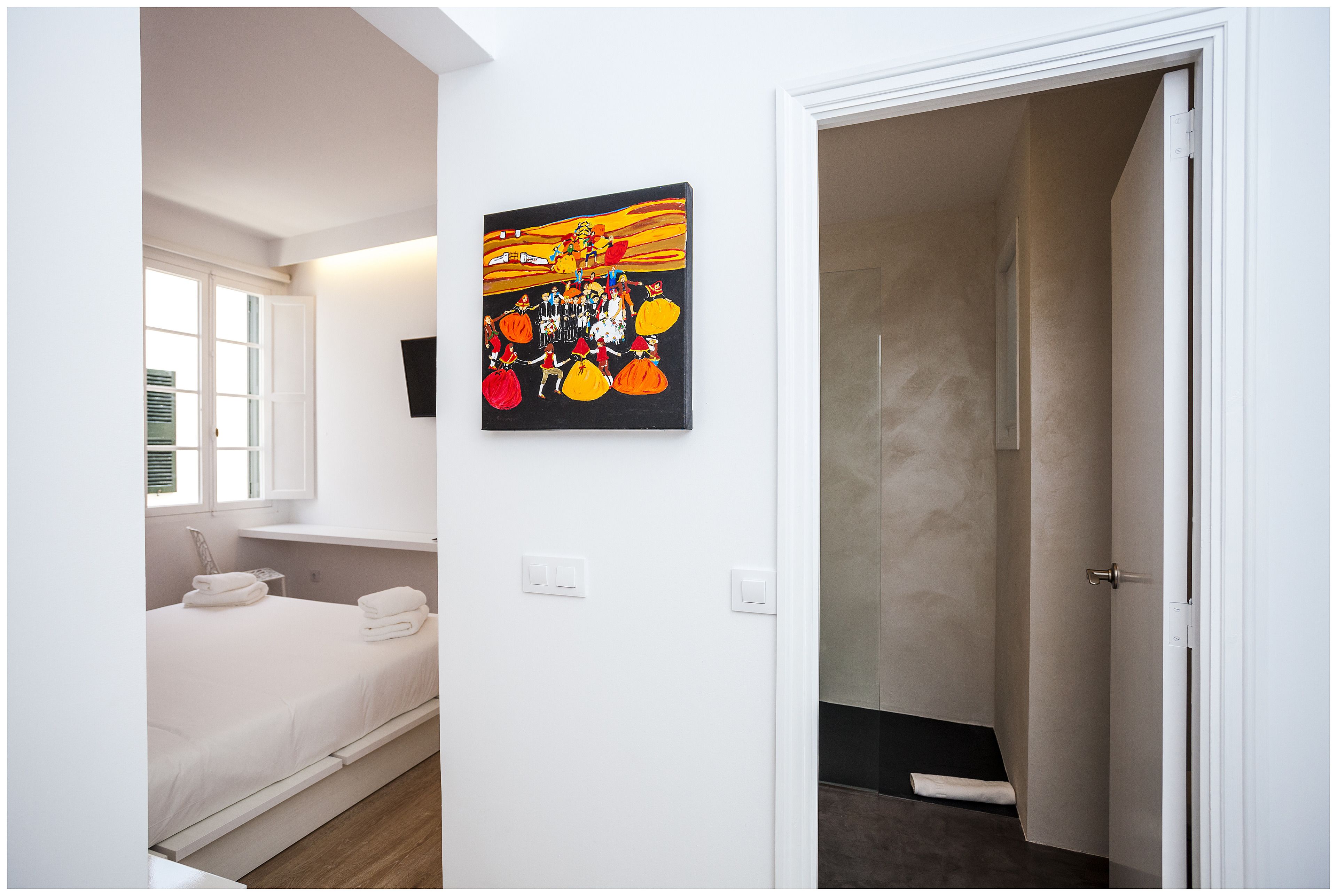A hotel room with a bed, a painting on the wall, and a bathroom visible through an open door.