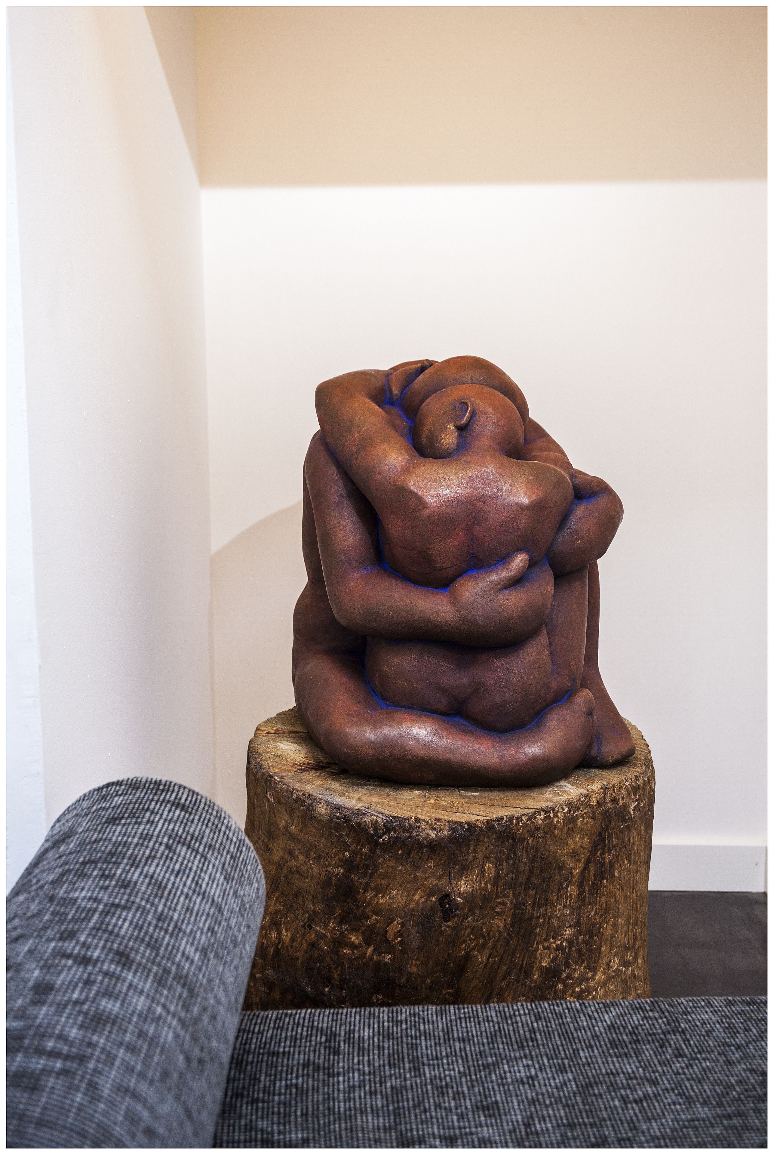 A sculpture of intertwined figures on a wooden stool in a room with a gray couch.