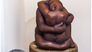 A sculpture of intertwined figures on a wooden stool in a room with a gray couch.