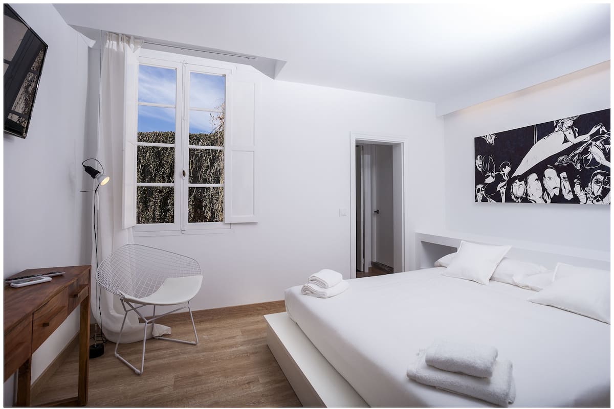 A bedroom with a large bed, a chair, a desk, and a window.