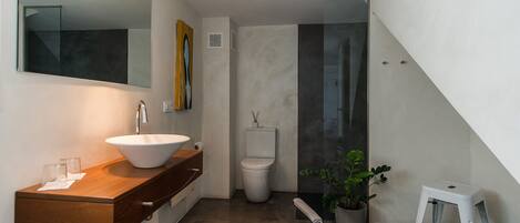 Un baño moderno con un espejo grande, un lavabo blanco, un inodoro y un taburete pequeño.