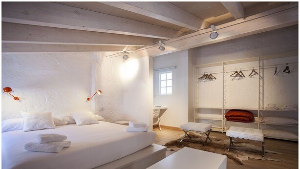 A modern bedroom with a large bed, bedside lamps, a bench, and a wardrobe with hangers. - Cheap & Chic Hotel (Ciutadella de Menorca)