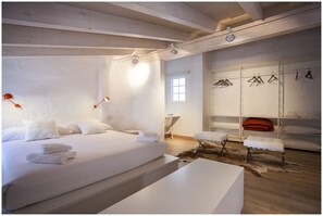 A modern bedroom with a large bed, bedside lamps, a bench, and a wardrobe with hangers. - Cheap & Chic Hotel (Ciutadella de Menorca)