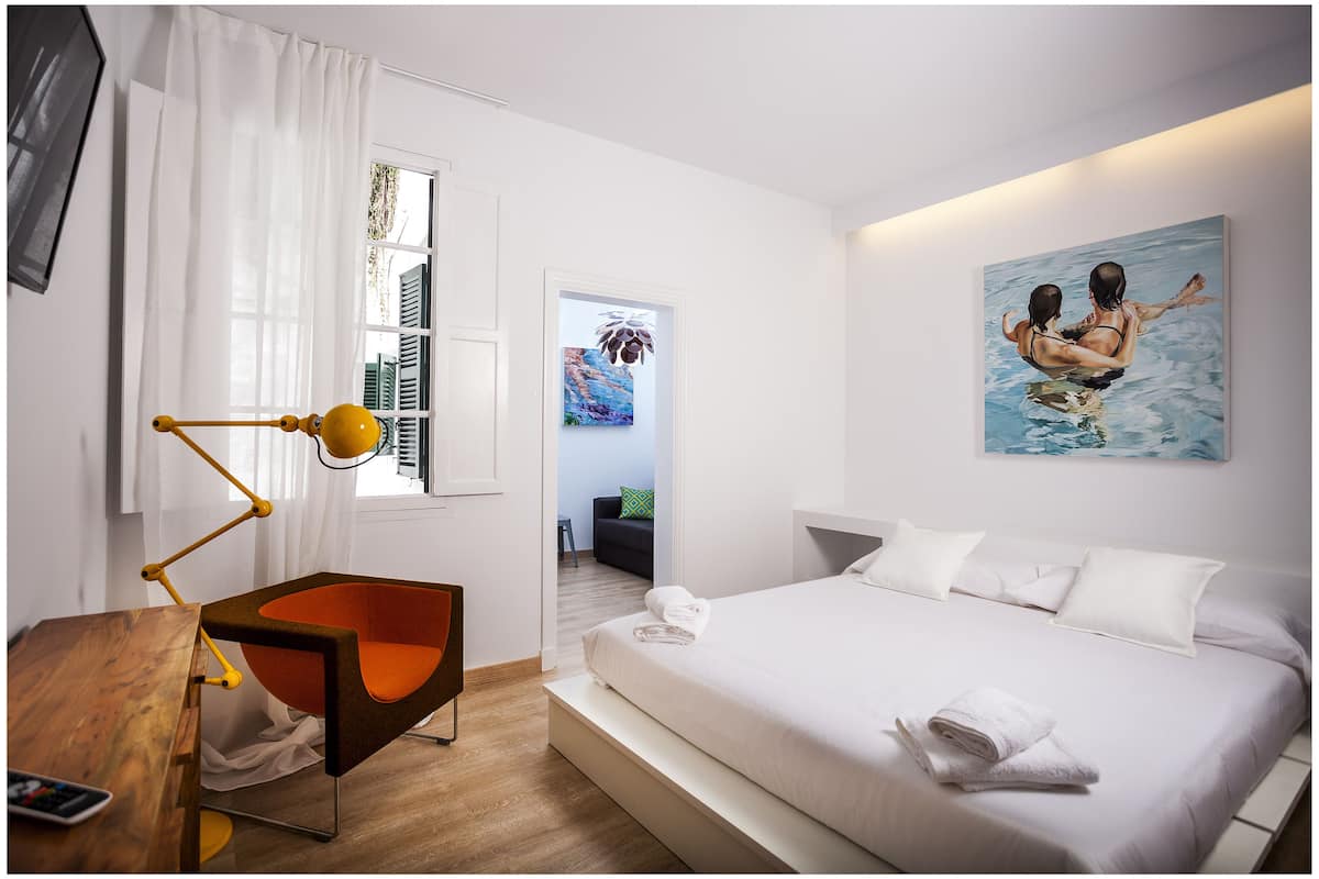 A modern hotel room with a bed, a desk, a chair, and artwork on the walls.