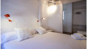 A bedroom with a large bed, two bedside tables, and a wardrobe with hanging clothes.
