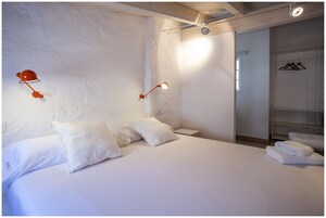 A bedroom with a large bed, two bedside tables, and a wardrobe with hanging clothes.
