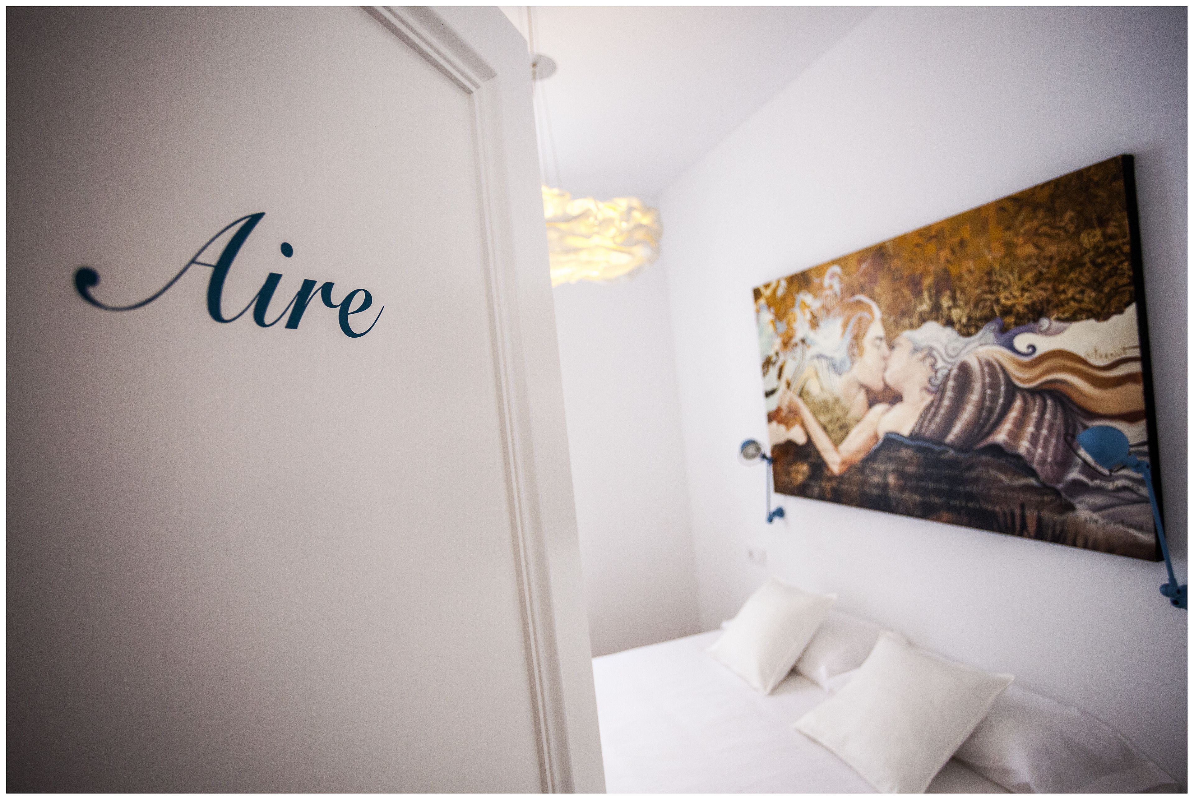 A bedroom with a bed, white pillows, a painting on the wall, and the word "Aire" written on the wall.