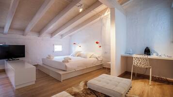 A modern bedroom with a bed, a desk, a TV, and a coffee maker.