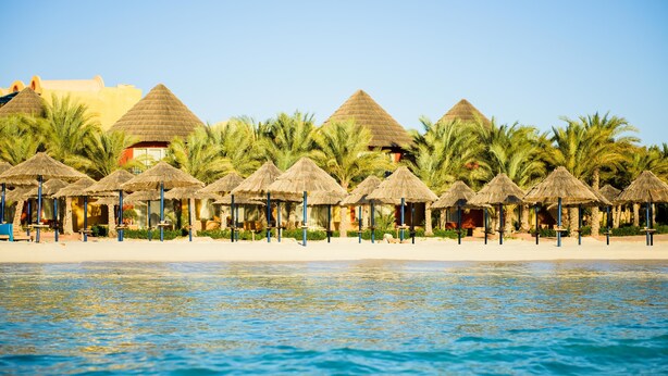 A beach resort with thatched-roof huts and palm trees. - Carols Beau Rivage Hotel (Marsa Matrouh)