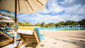 A poolside area with lounge chairs and umbrellas, a clear sky, and palm trees. - Carols Beau Rivage Hotel (Marsa Matrouh)