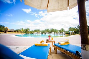 A poolside area with lounge chairs and a table, a clear blue sky, and palm trees in the background.