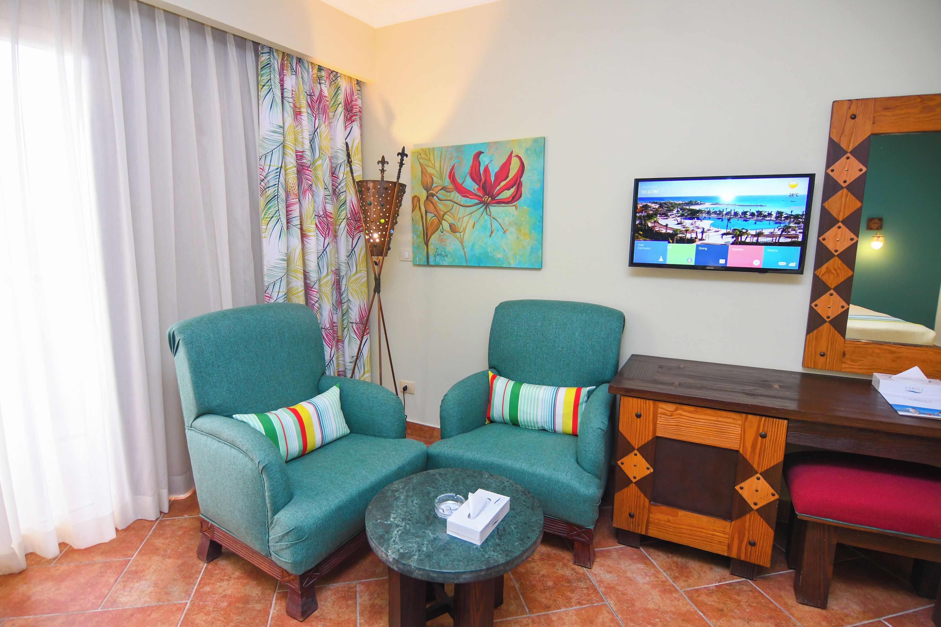 Una habitación con dos sillones color turquesa, una mesita redonda pequeña, un mueble de madera, un cuadro y un televisor en la pared.