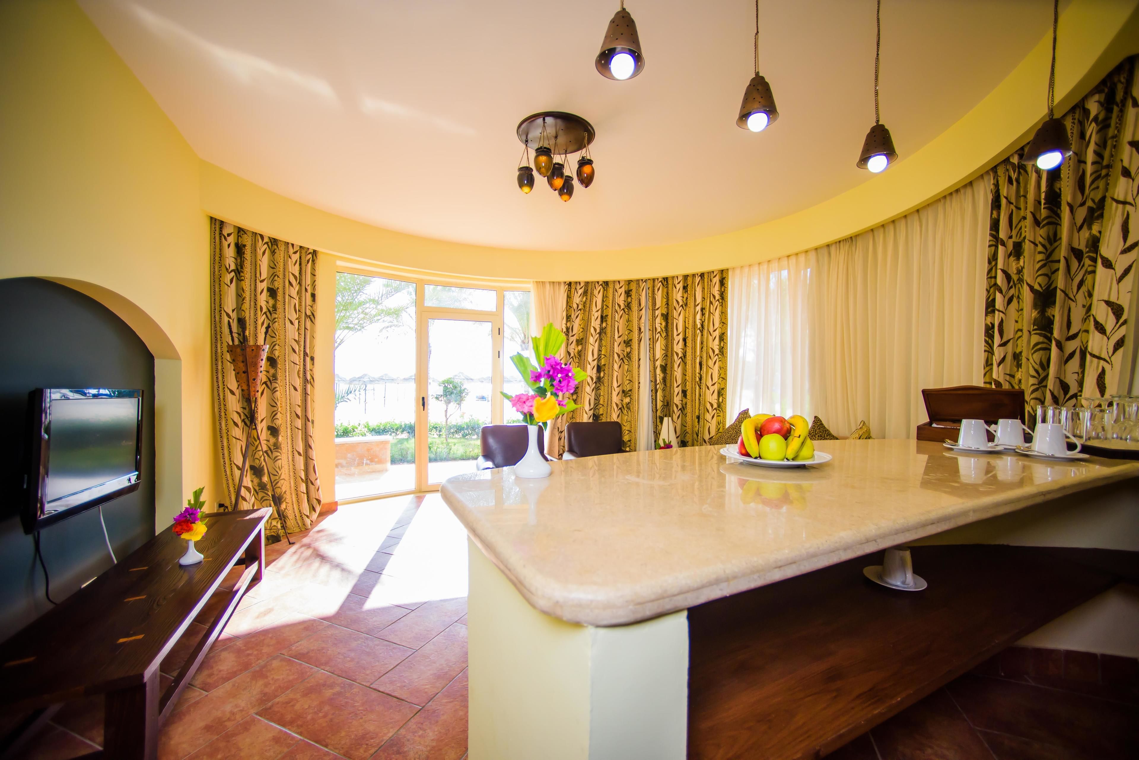 Uma cozinha moderna com uma ilha central, uma área de refeições com cadeiras, uma televisão e uma grande janela com cortinas.