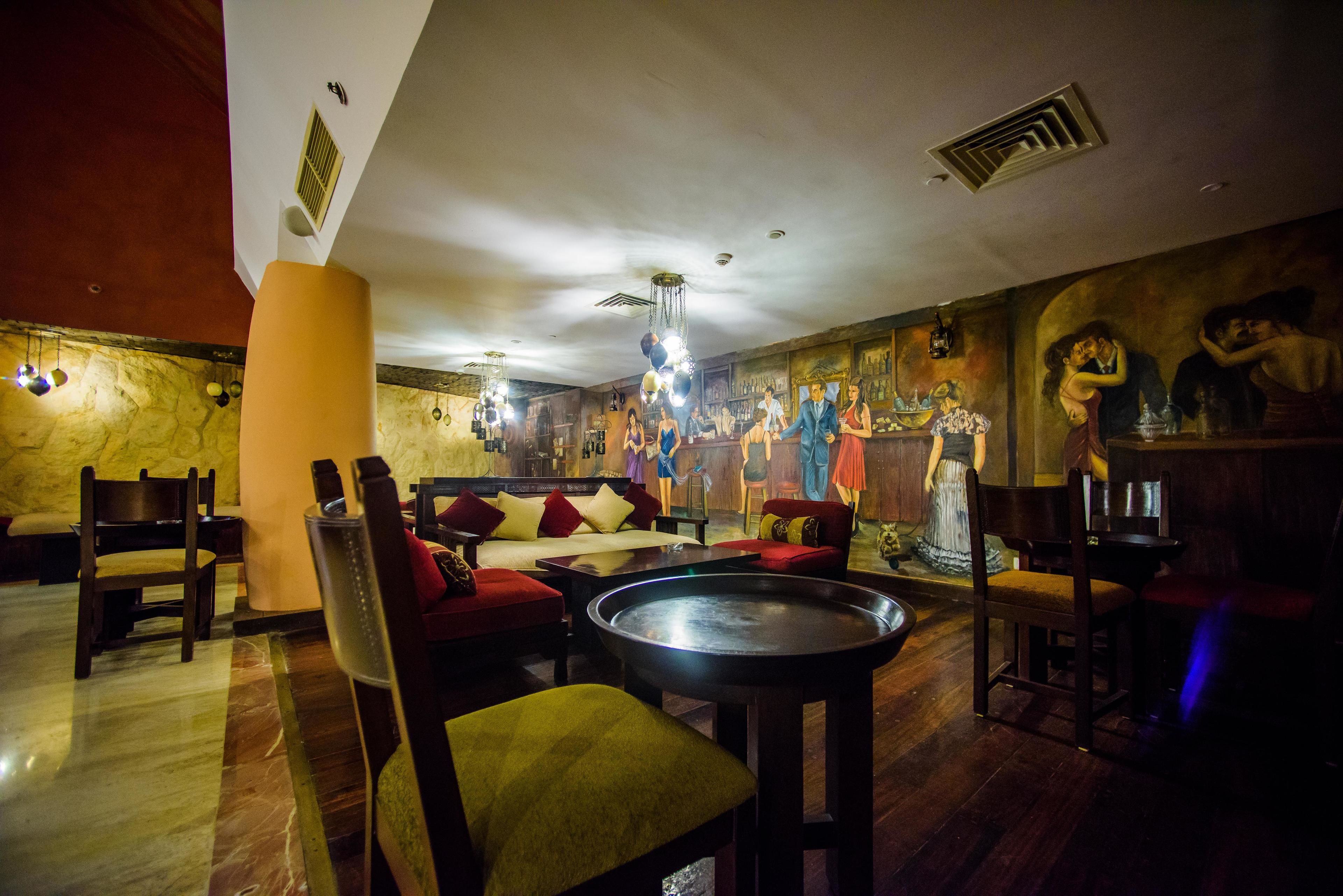 Un'area lounge scarsamente illuminata, con pavimento in marmo, arredi in legno e un grande murale.