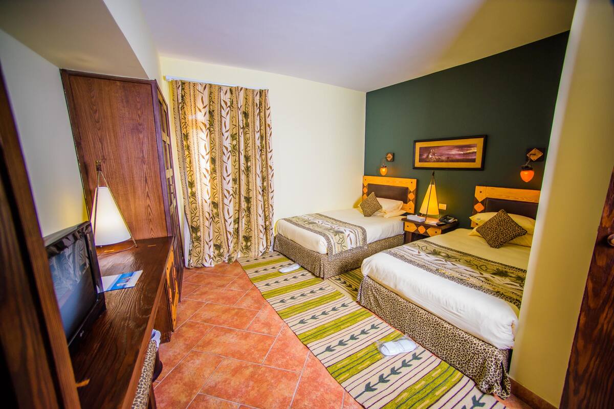 Camera d'albergo con due letti, una TV e una scrivania in legno.