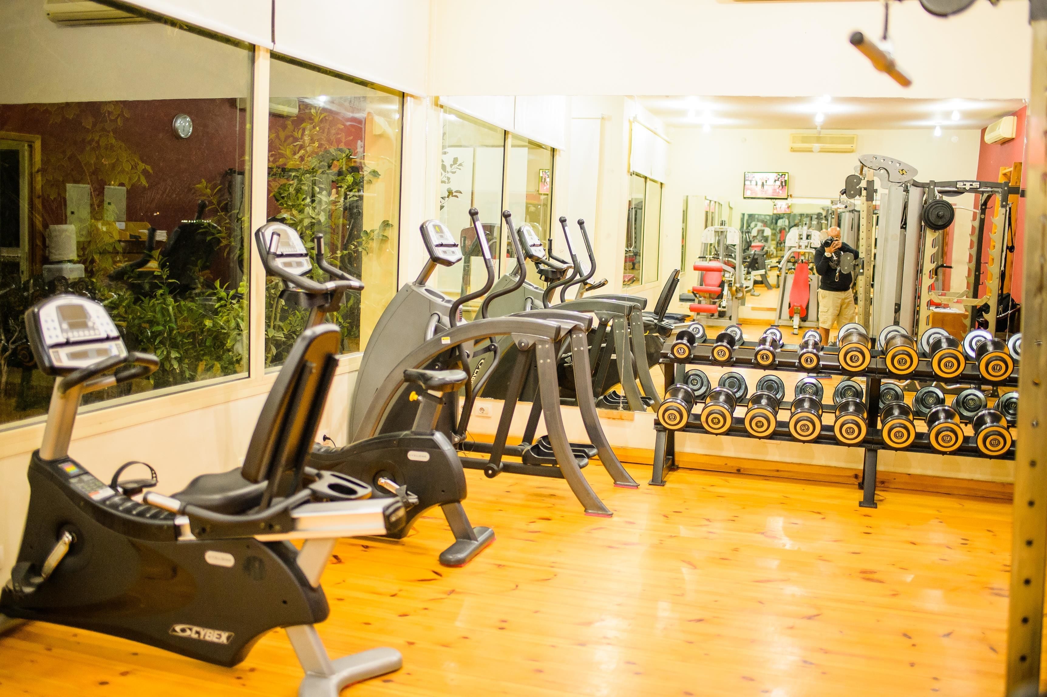 Una palestra con macchinari cardio, rastrelliere per pesi e uno specchio che riflette l'attrezzatura.