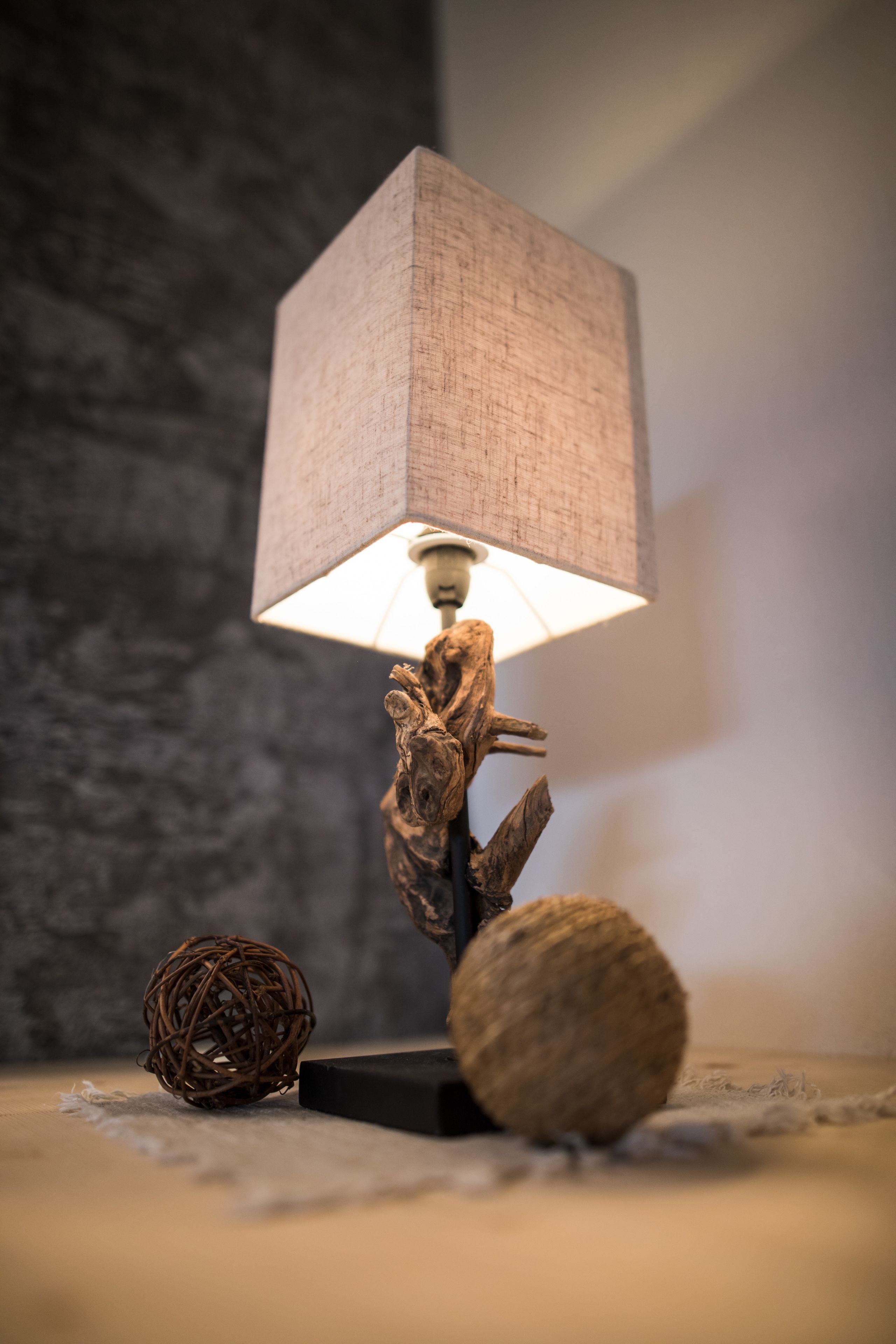A table lamp with a square shade and a decorative base, placed on a textured surface with two spherical objects beside it.