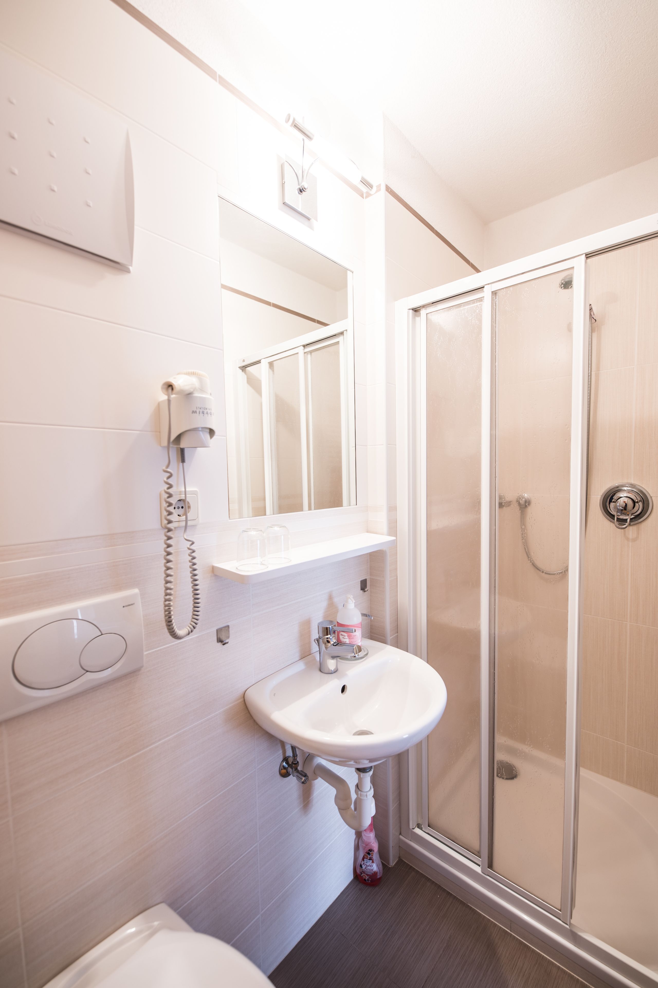A bathroom with a white sink, a mirror, a hairdryer, and a glass-enclosed shower.