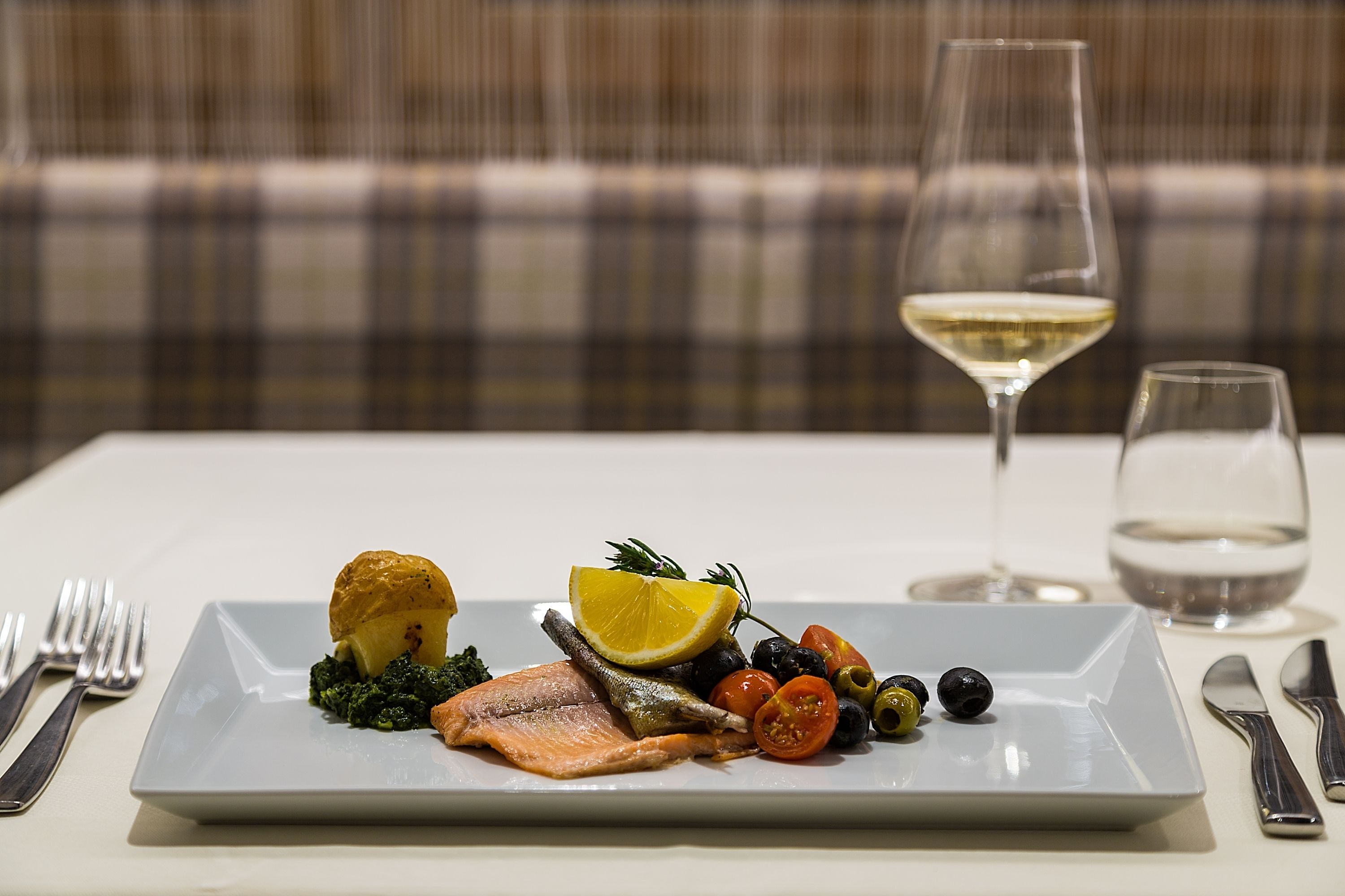 A plate of food with salmon, vegetables, and a lemon wedge on a white table.