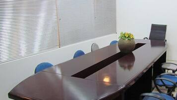 Un salón de conferencias con una larga mesa, sillas azules y un jarrón con flores amarillas.