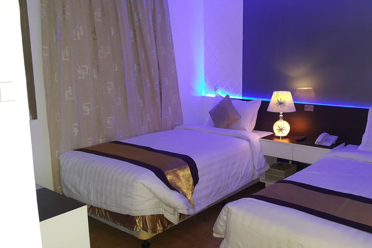 A hotel room with two beds, a bedside table with a lamp, a phone, and a mirror.