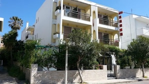 A multi-story building with balconies, a stone wall, and greenery in front. - Karis Hotel (Kos)