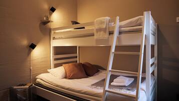 Una cama individual con escalera, una mesita de noche con lámpara y un estante en la pared con un vaso y un libro.