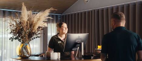 A reception desk with a computer, a vase with dried plants, and a coffee cup.