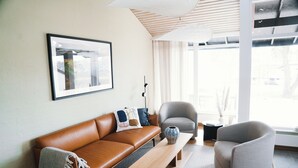 Uma sala de estar moderna com um sofá de couro marrom, uma poltrona cinza, uma mesa de centro de madeira e um quadro pendurado na parede.