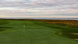 A golf course with a flagstick, well-maintained grass, and a distant view of the sea. - Barsebäck Resort Hotell (Loddekopinge)