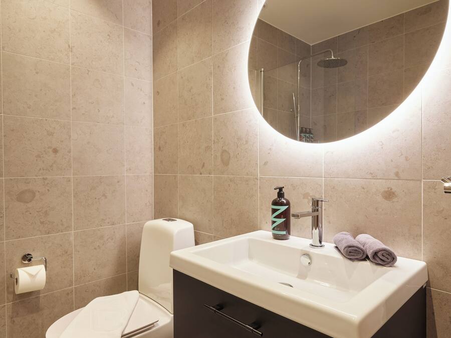 A bathroom with a round mirror, a white sink, a dark cabinet, and a toilet with a towel on it.