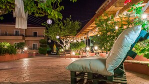 A patio area with a wooden bench and a cushion, surrounded by potted plants and a pergola with string lights. - Babis Studios (Zakynthos)