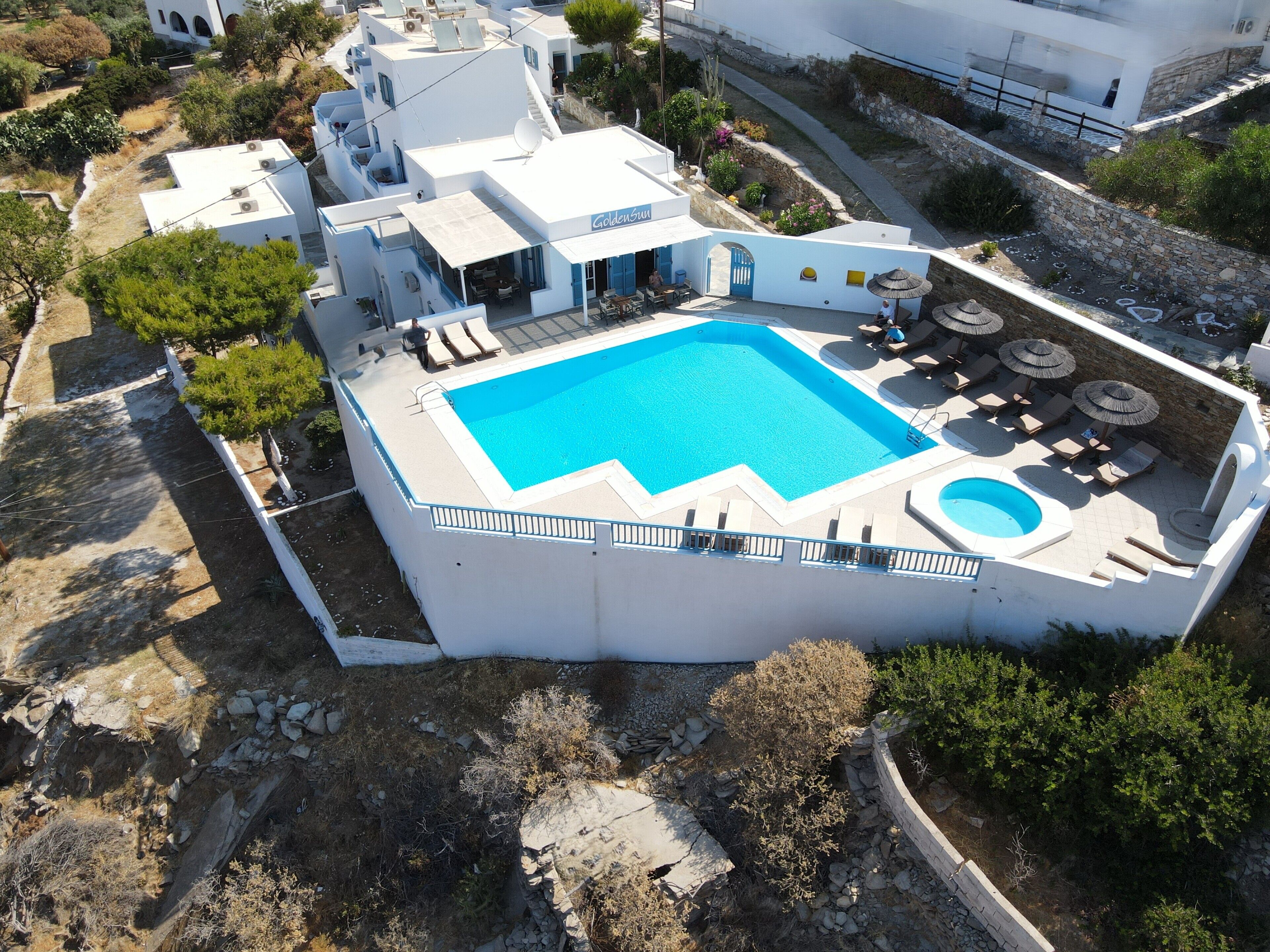 A white building with a swimming pool, outdoor seating, and a small garden area.