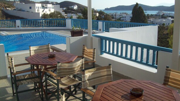 A terrace with a pool, wooden furniture, and a view of the sea and buildings. - Golden Sun Hotel (Ios)