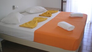 A neatly made bed with white and orange linens, a yellow towel, and a white towel. - Golden Sun Hotel (Ios)