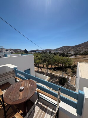 Un balcon avec une table et des chaises, donnant sur un paysage composé d’arbres et de bâtiments.