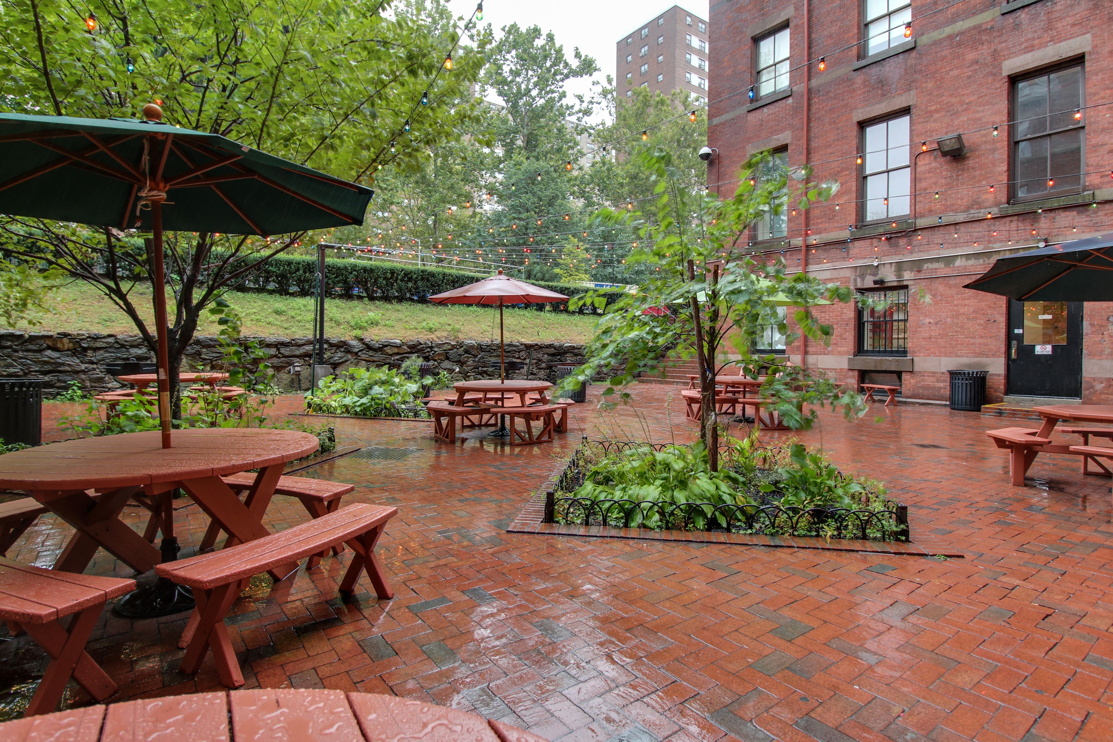 An outdoor patio with brick flooring, picnic tables, and umbrellas.