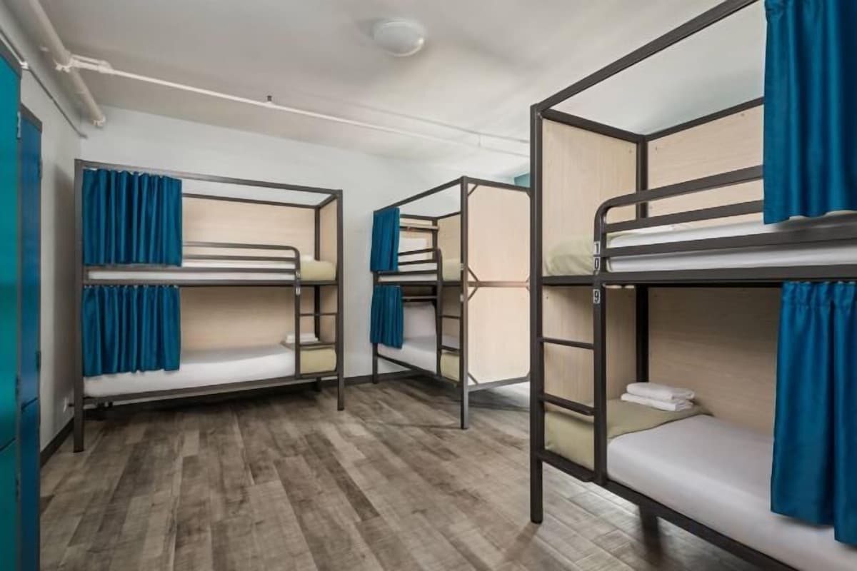 Une chambre avec des lits superposés, un plancher en bois et des rideaux bleus.