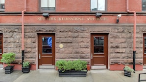 Exterior del New York International AYH-Hostel con fachada de piedra, dos puertas marrones y macetas negras con follaje.