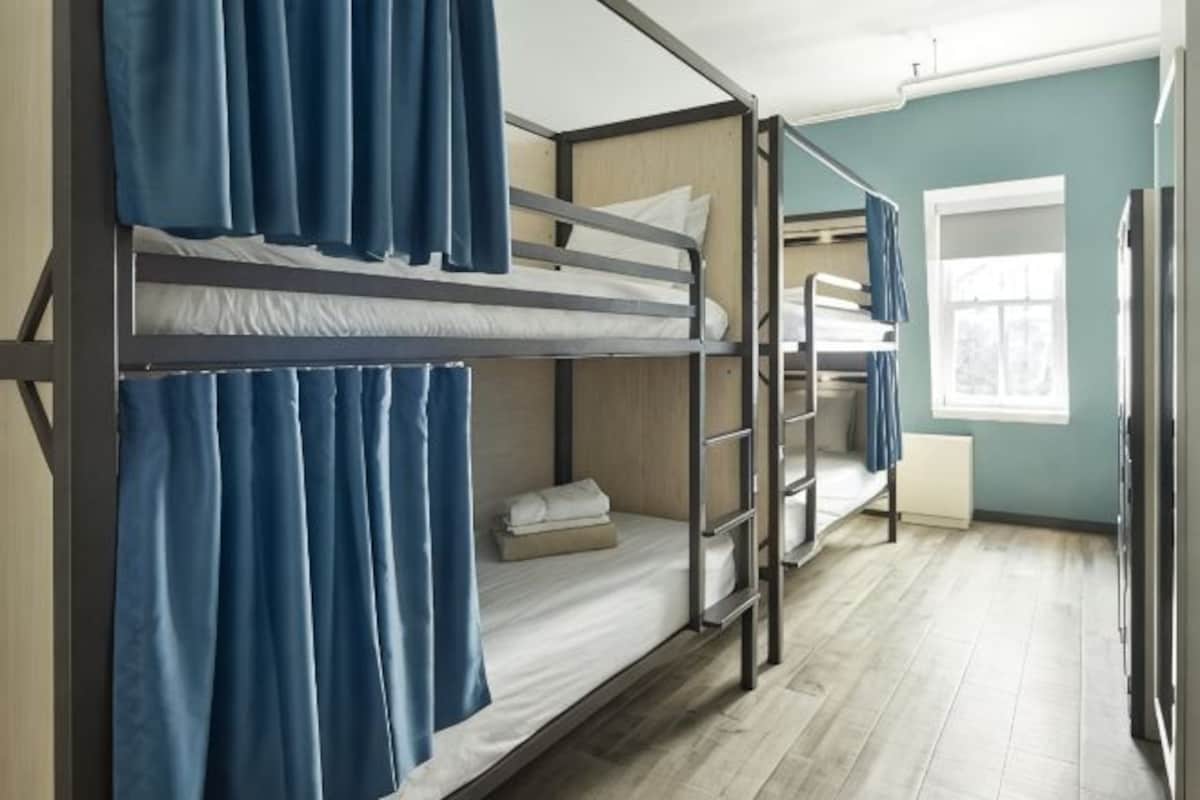 Une chambre avec un lit superposé, des rideaux, une fenêtre et un radiateur.