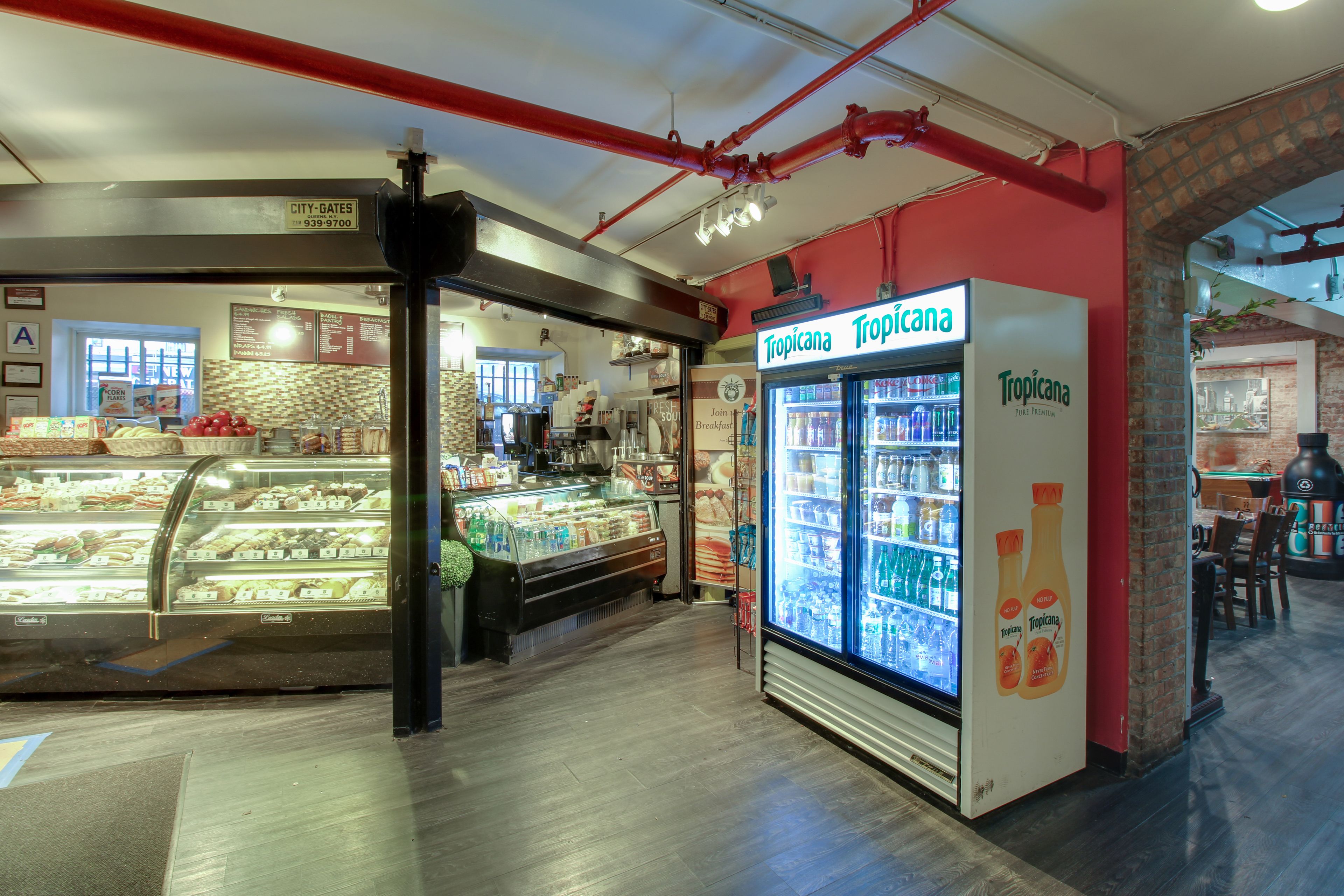 Un expositor de panadería con diversos productos horneados, un expositor refrigerado con bebidas y una zona de estar con mesas y sillas.