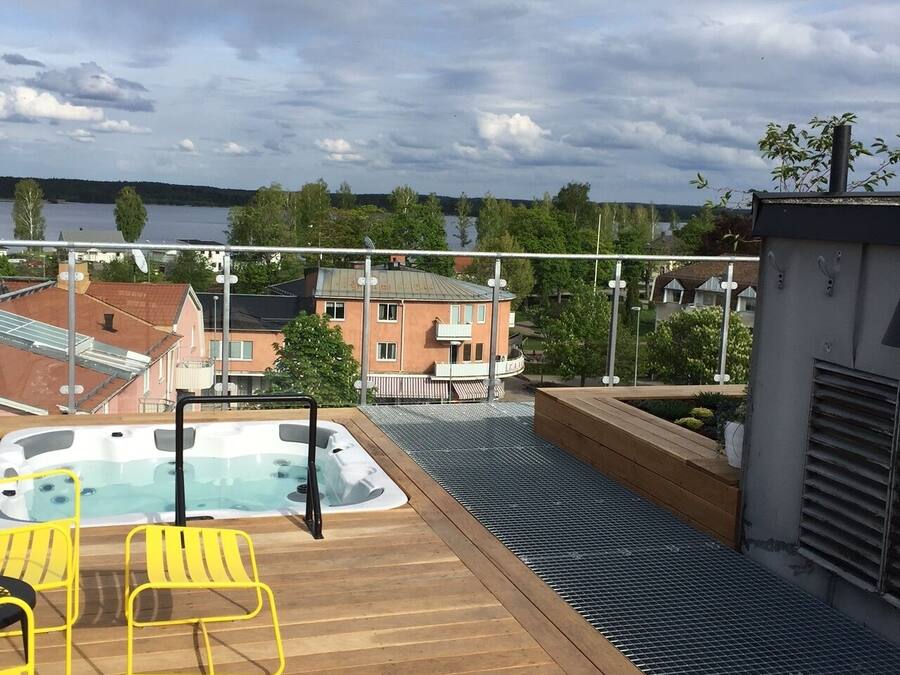 Une terrasse sur le toit avec un jacuzzi, des chaises jaunes et une vue sur un lac et des bâtiments.