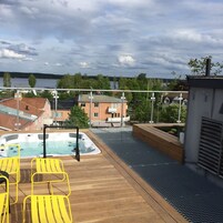 Terraza en la azotea con jacuzzi, sillas amarillas y vistas a un lago y edificios.