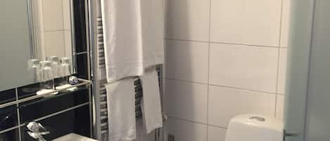 A bathroom with a white sink, mirror, and toilet. There is a towel rack with towels, a glass shower enclosure, and a toilet paper holder.