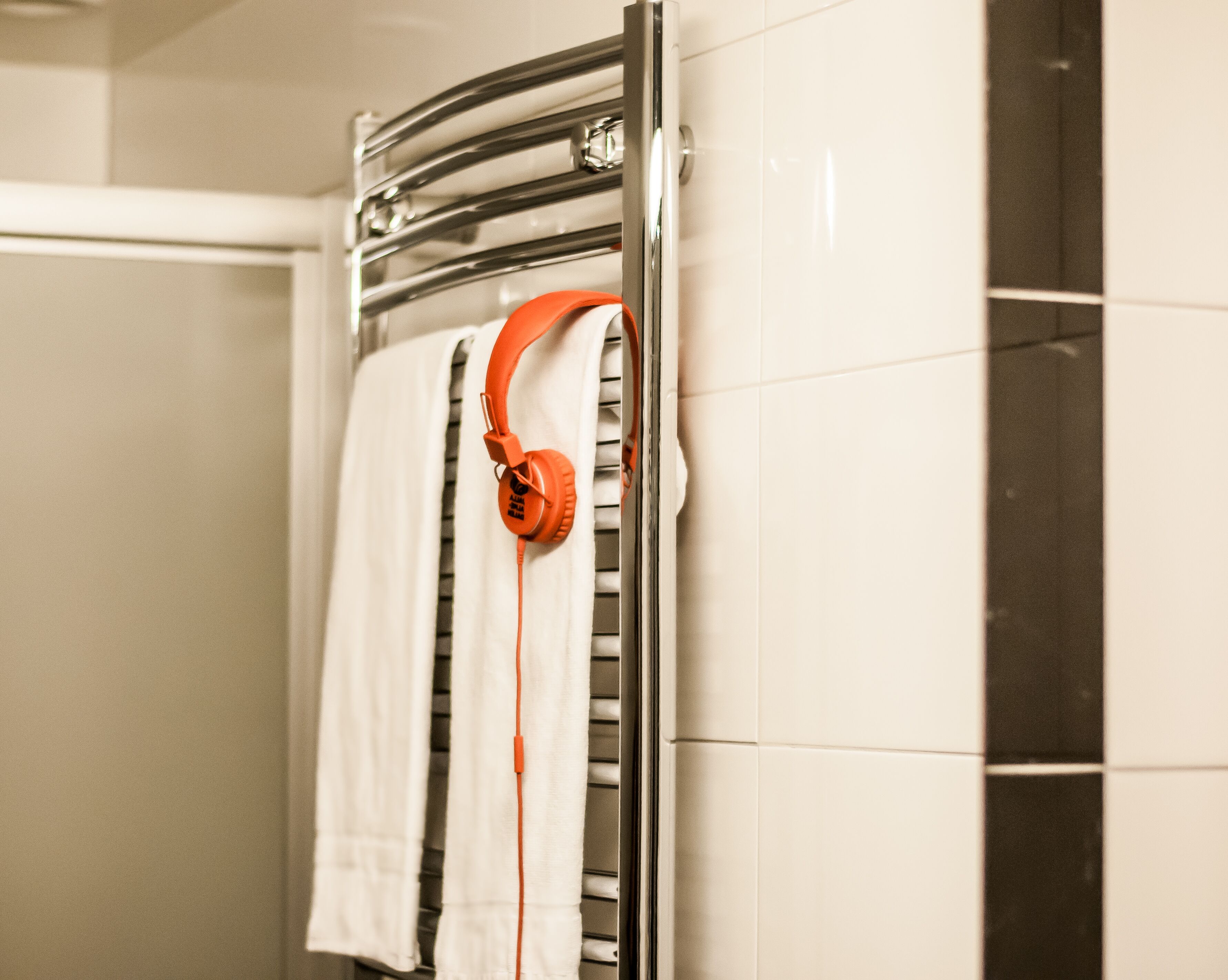 Une salle de bain avec un porte-serviettes sur lequel est posée une serviette blanche et une paire d’écouteurs orange.