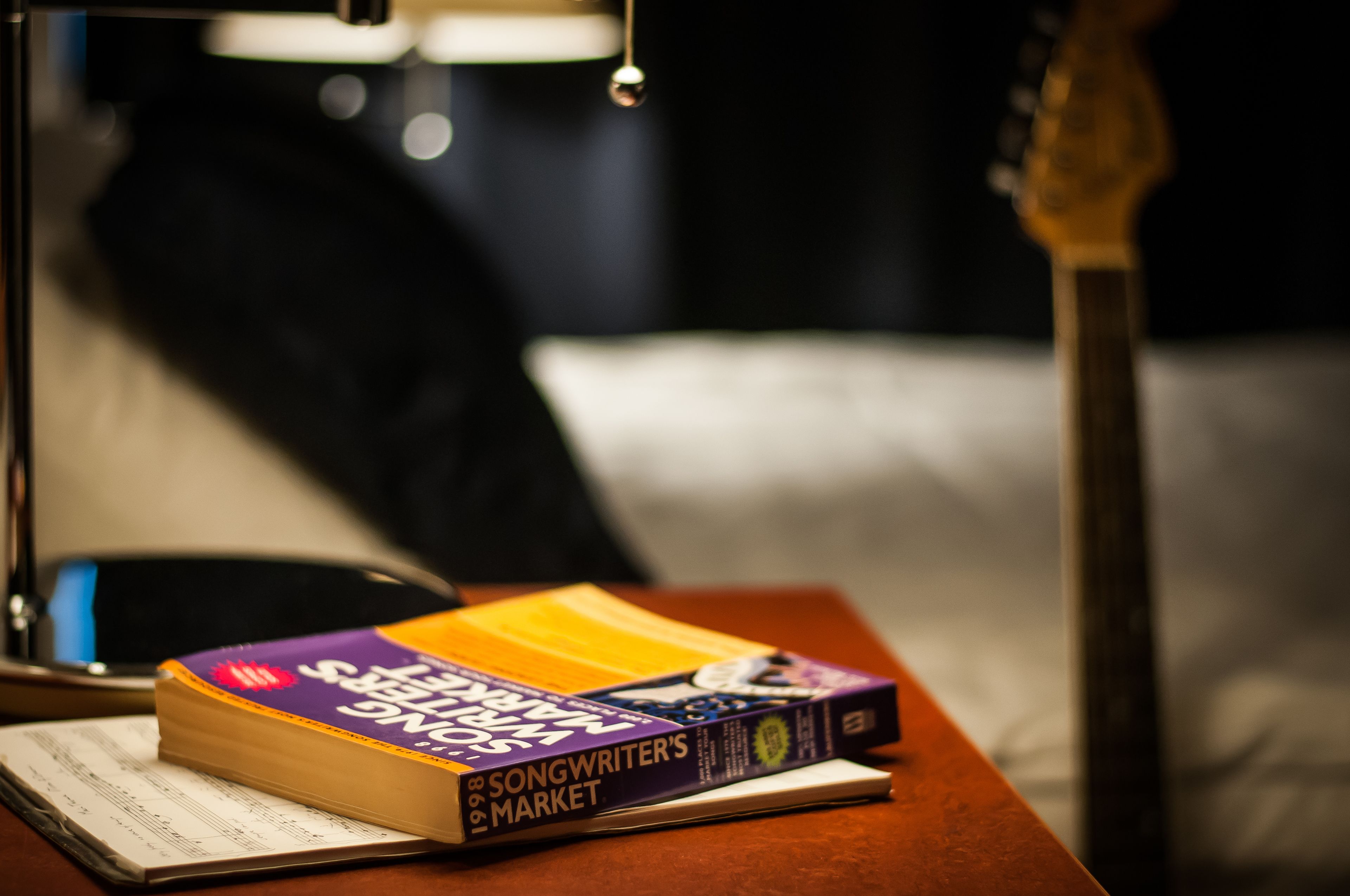 Un livre intitulé « Le guide du compositeur-interprète » est posé sur une table en bois, avec une guitare en arrière-plan.