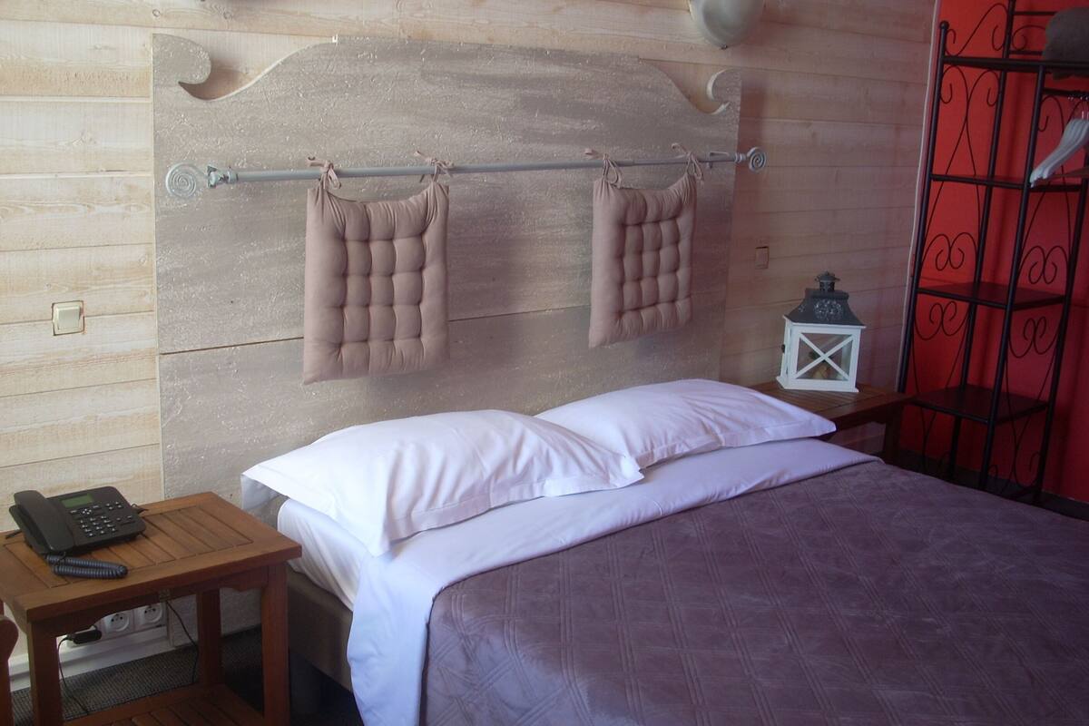A bed with a headboard, pillows, a bedside table with a phone, and a red metal gate.
