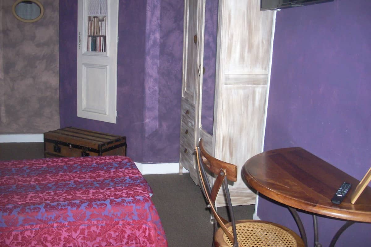 A room with a bed, a small table, a chair, a suitcase, and a television mounted on the wall.
