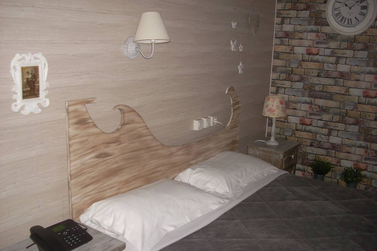 A bedroom with a wooden headboard, a bedside phone, a wall clock, and a brick-patterned wall.