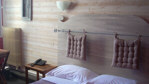 Quarto com cabeceira de madeira, mesa de cabeceira com telefone e cama com roupa de cama branca e roxa.